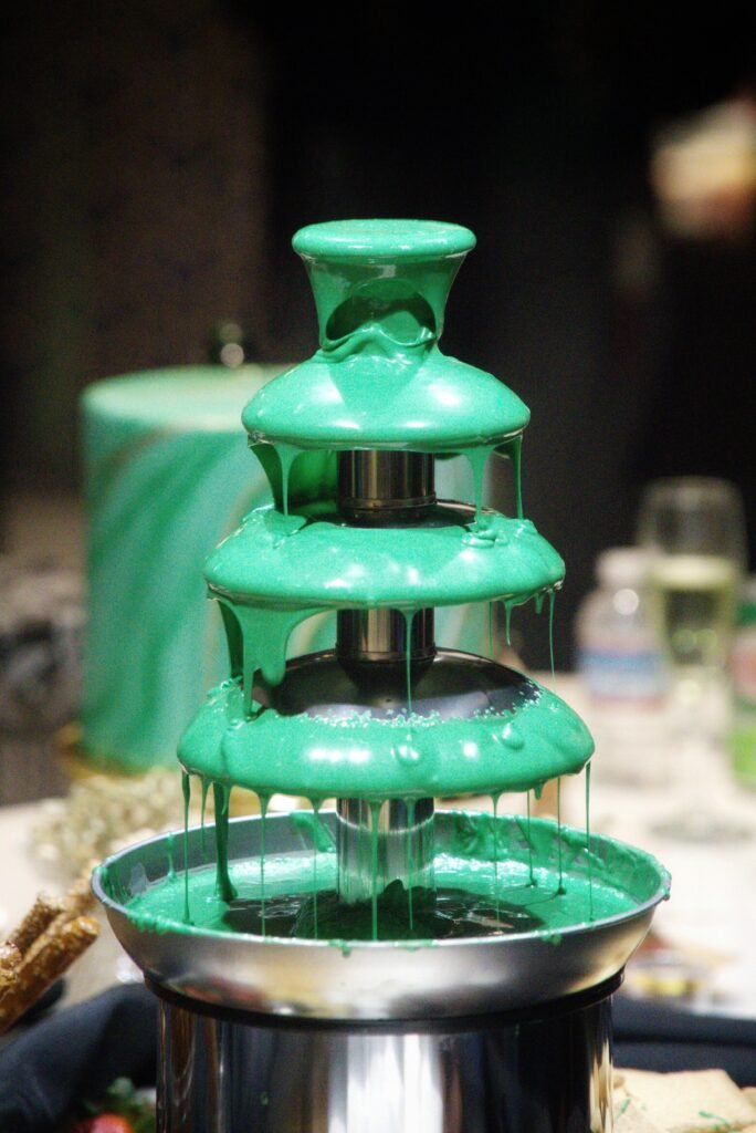 A vibrant green fondue fountain with melted chocolate at an elegant indoor event.